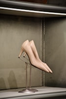 A pair of elegant high-heeled shoes displayed on a metal stand against a soft, green textured background with metallic studs outlining the edge.