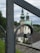 A metal railing with a decorative spiral design is in the foreground, with a blurred background featuring a church with two green-domed towers. The sky is overcast, and there is greenery to the left side of the image.