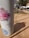 A tumbler adorned with various stickers stands on a wooden picnic table. Sunlight casts shadows across the table, with a blurred background featuring cars and trees.