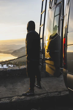 A man standing beside his van on a mountain overlook during golden hour.