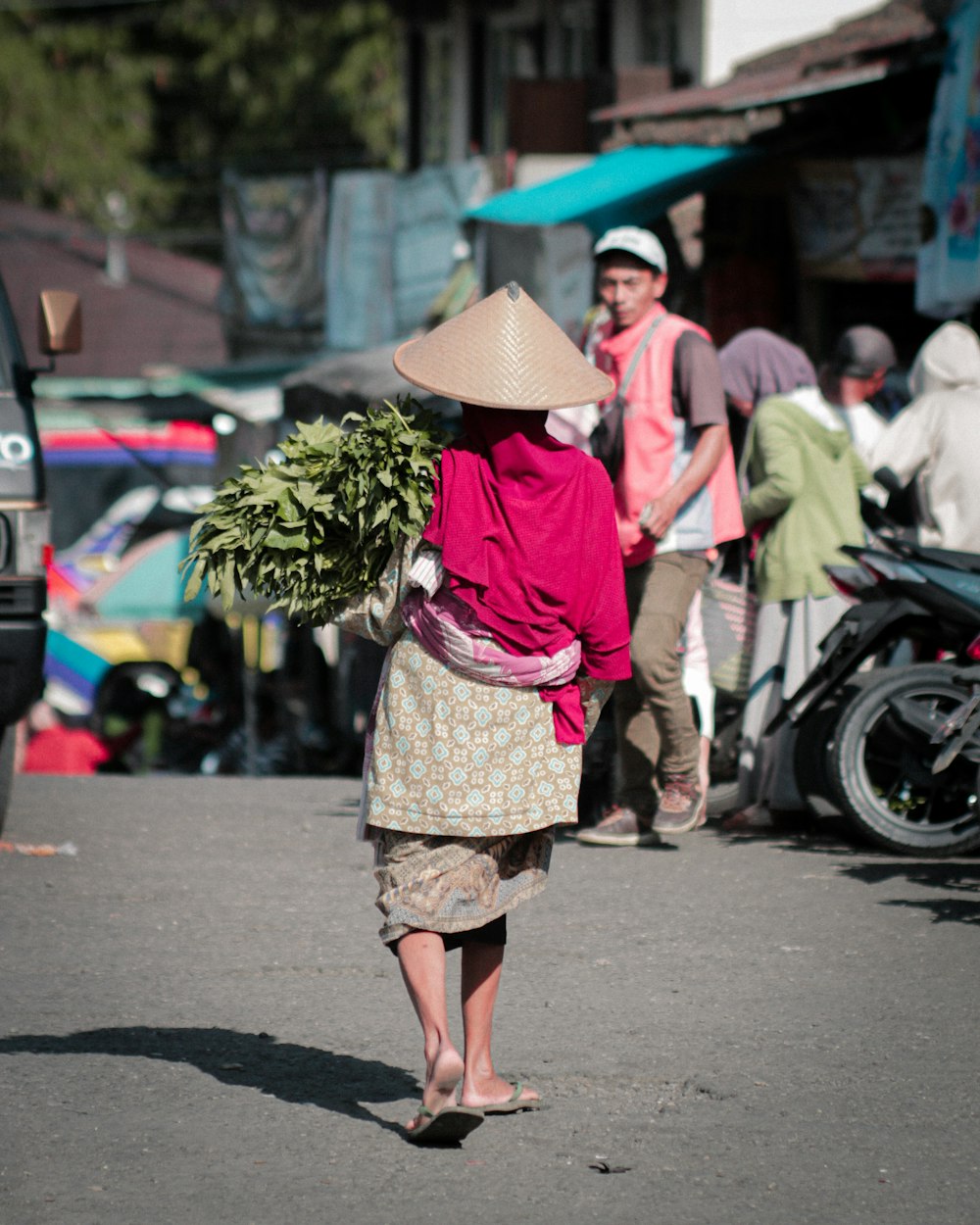 a woman walking down a street carrying a bunch of plants