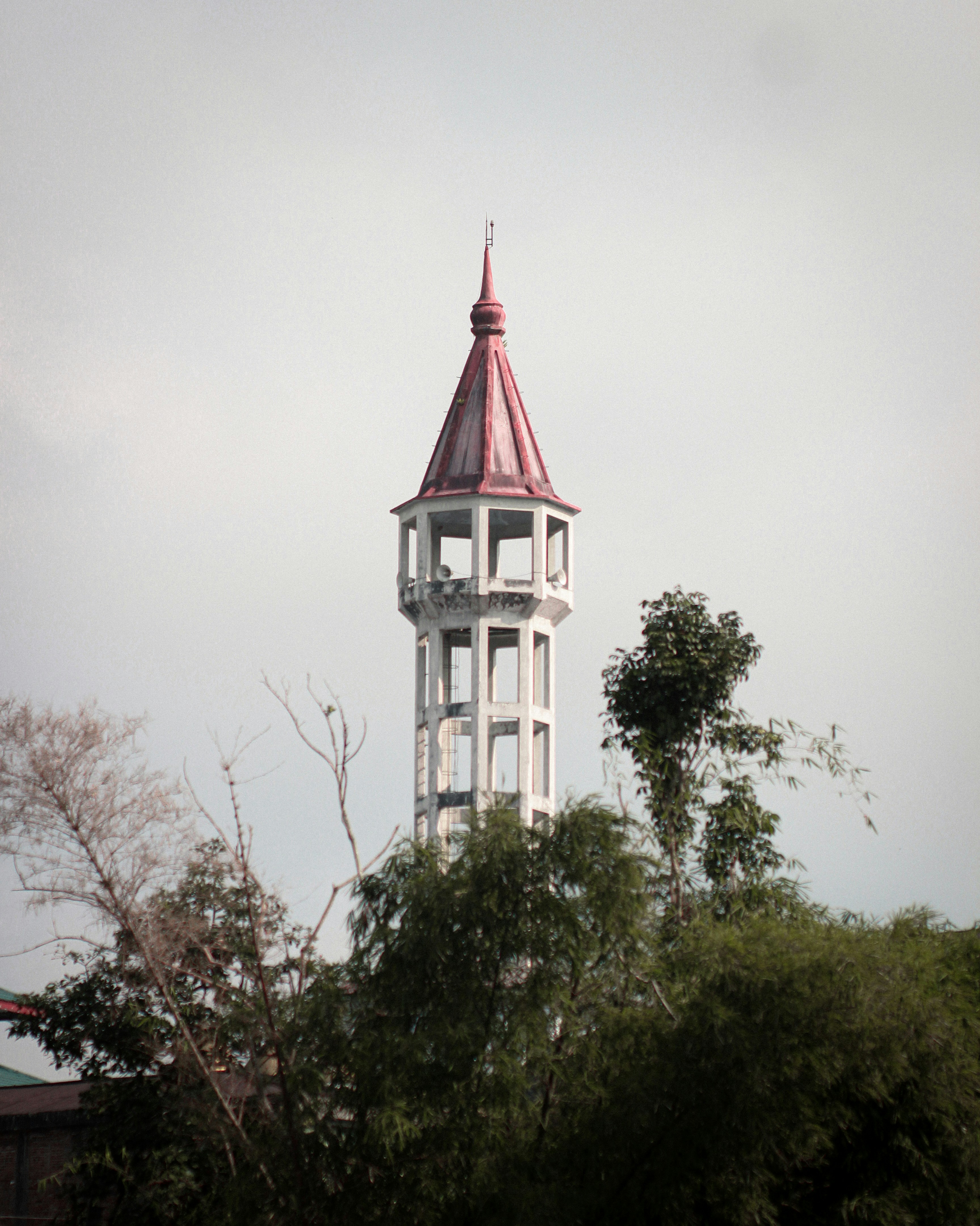 a white tower with a red roof surrounded by trees