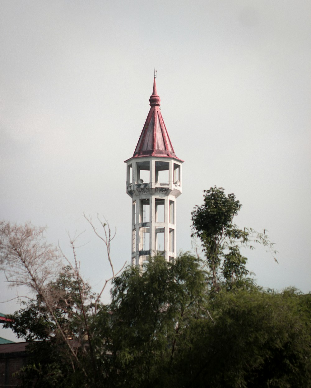 Una torre bianca con un tetto rosso circondato da alberi