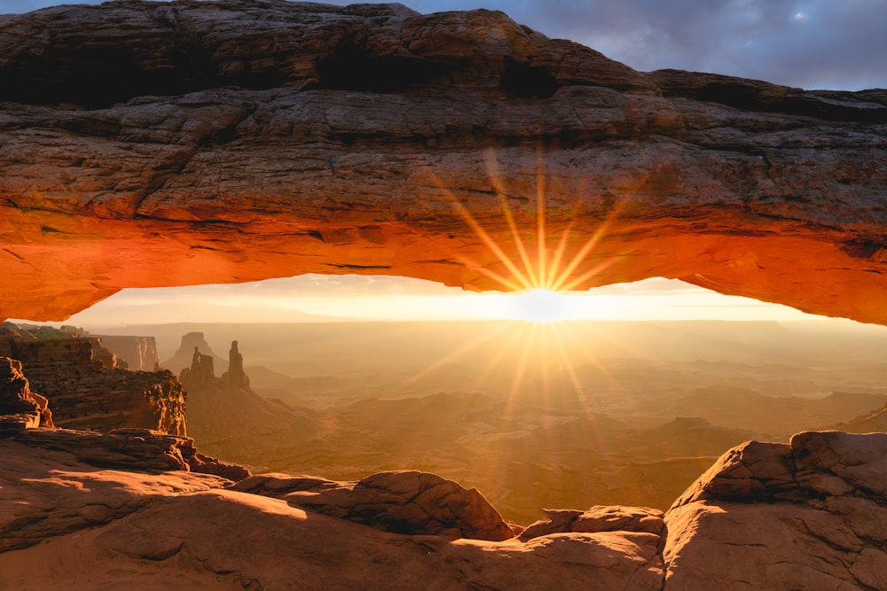 the sun is shining through an arch in the desert