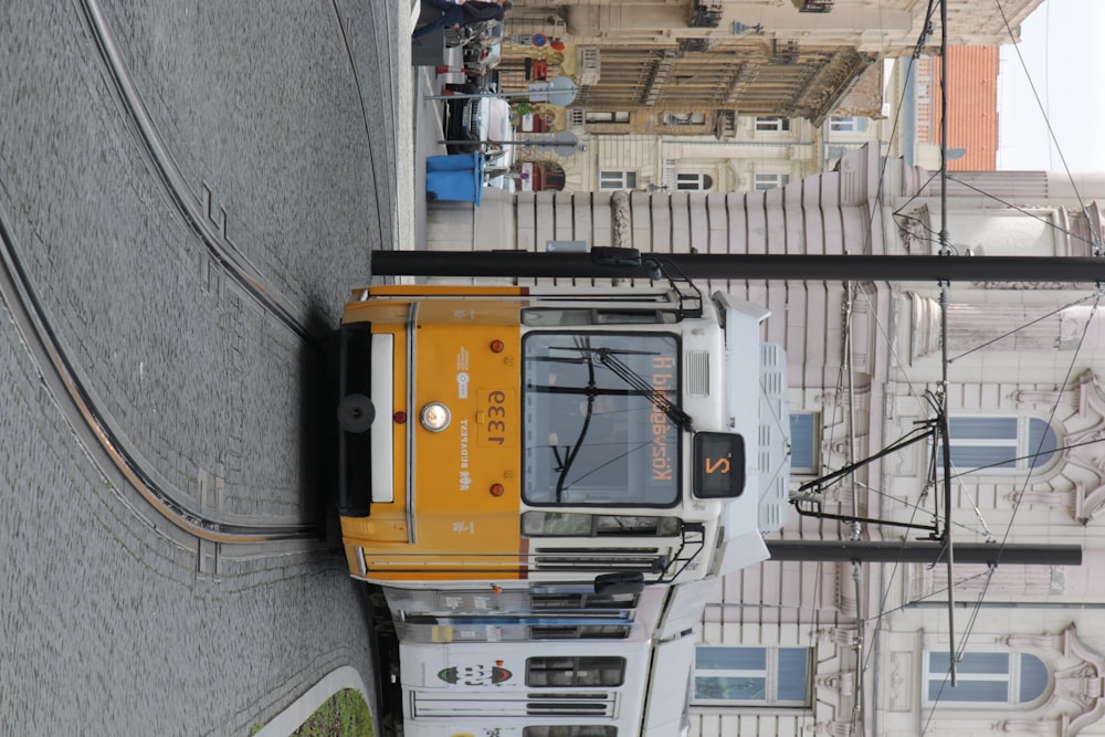 a yellow and white train traveling down a street next to a tall building