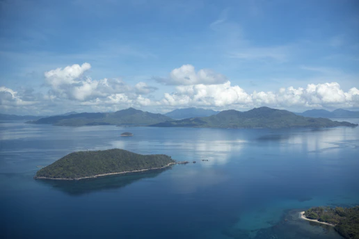 A serene sunrise view over the crystal-clear waters surrounding Pulau Peling, with lush green islands in the distance.