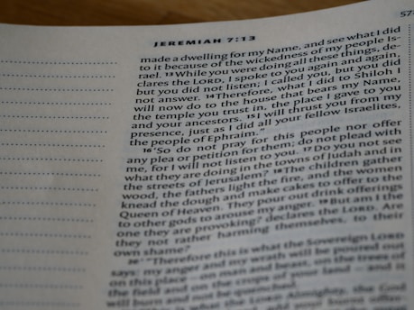 A close-up image of a Bible page showing text from the book of Jeremiah. The verses include Jeremiah 7:13 to 7:20, with legible text in a standard format. The page has a column on the left side with dotted lines, possibly for notes. The paper appears to be slightly textured, and the text is in black font.