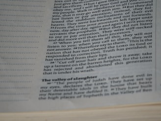 The image features a close-up view of a page from a book with text on it. The text is printed in black ink on an off-white page and contains paragraphs with different sections and headings.