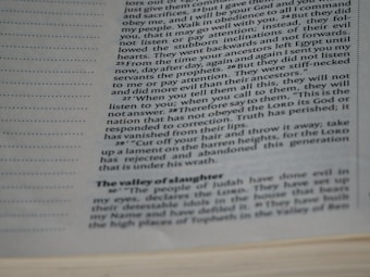 The image features a close-up view of a page from a book with text on it. The text is printed in black ink on an off-white page and contains paragraphs with different sections and headings.