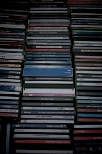 A collection of stacked CD cases, neatly organized in rows with visible labels and album information. The cases exhibit a range of colors and some wear, suggesting a diverse music collection.