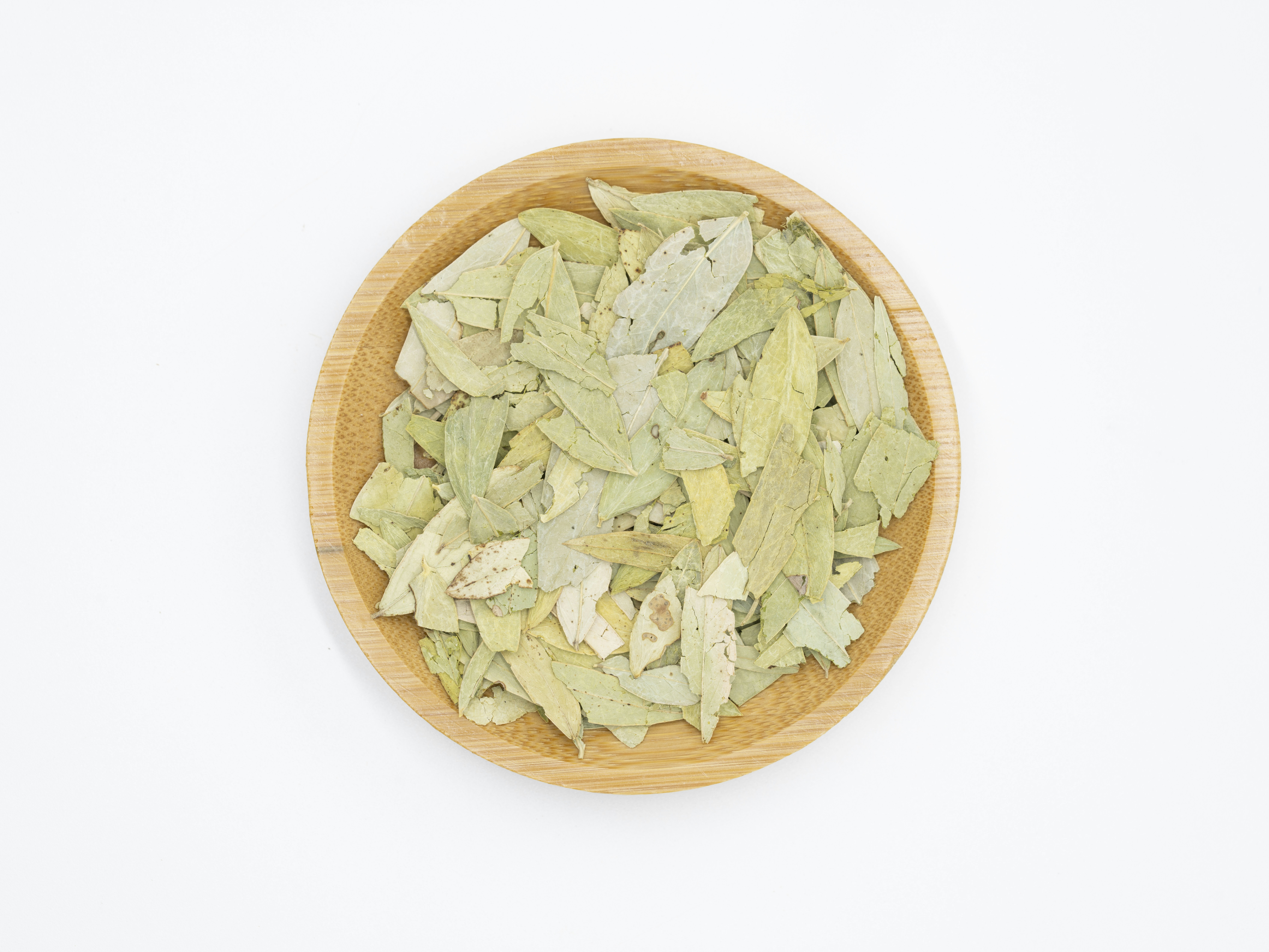 eine mit Blättern gefüllte Holzschale auf einem weißen Tisch