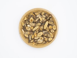 A wooden plate filled with sliced, dried herbal roots displaying various shades of brown and beige, arranged neatly against a plain white background.