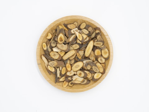 A wooden plate filled with sliced, dried herbal roots displaying various shades of brown and beige, arranged neatly against a plain white background.