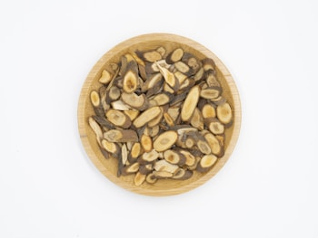 A wooden plate filled with sliced, dried herbal roots displaying various shades of brown and beige, arranged neatly against a plain white background.