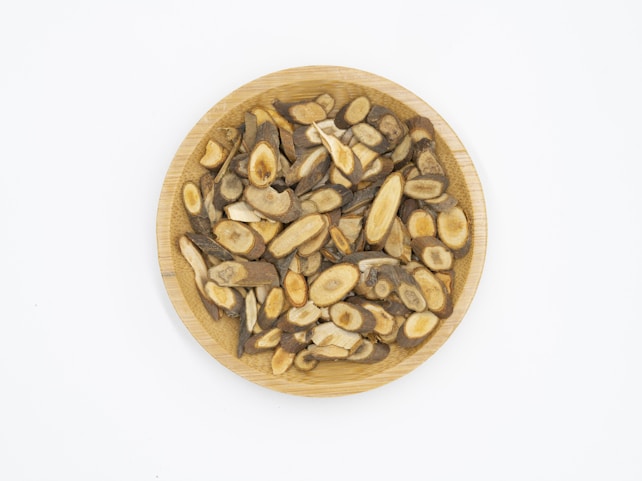 A wooden plate filled with sliced, dried herbal roots displaying various shades of brown and beige, arranged neatly against a plain white background.