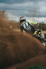 A powerful shot of a motocross rider kicking up dust on a rugged forest trail under moody, dark skies.