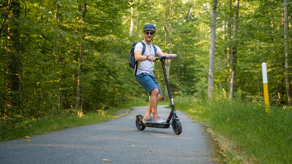 a man riding a scooter down a road in the woods