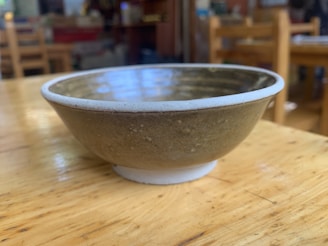 Close-up of a smooth, earth-toned ceramic bowl resting on a wooden table.