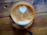 A close-up of a steaming latte art heart in a delicate ceramic cup on a polished wooden table.