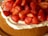 A delicious-looking cake topped with freshly sliced strawberries and a layer of cream. The strawberries are vibrant and glossy, suggesting ripeness and freshness.