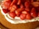 A delicious-looking cake topped with freshly sliced strawberries and a layer of cream. The strawberries are vibrant and glossy, suggesting ripeness and freshness.