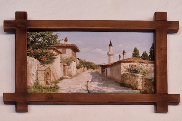 An old oil painting in a gilded frame depicting a serene European countryside scene.