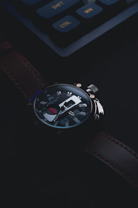 Close-up of a luxury watch rim-lit against a textured dark leather background, highlighting gold accents.