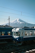 a blue and white train traveling past a snow covered mountain