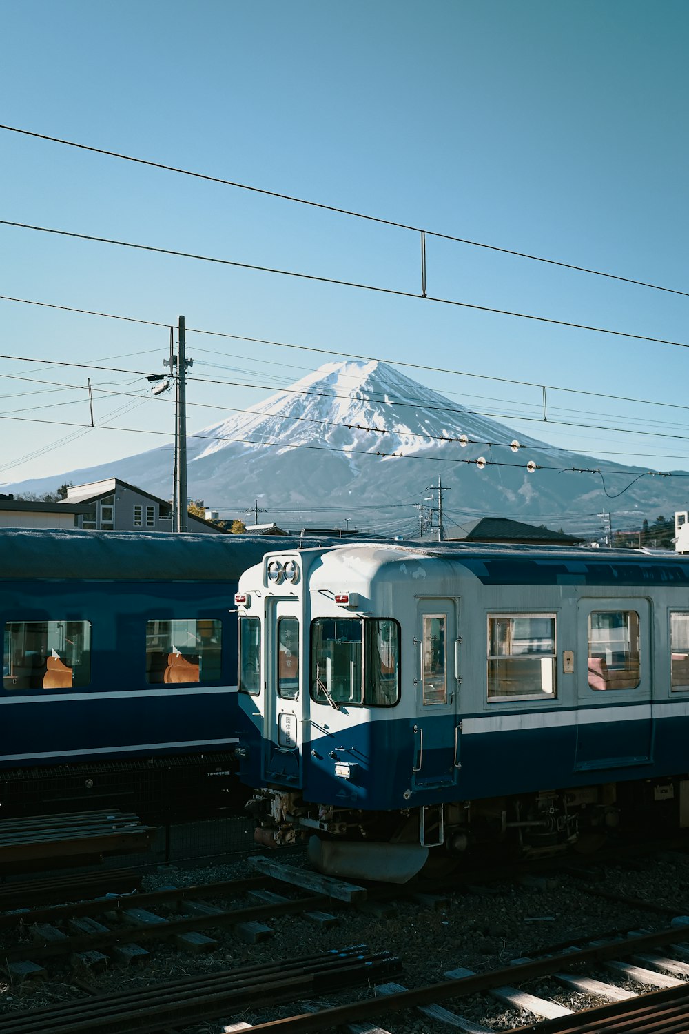 a blue and white train traveling past a snow covered mountain
