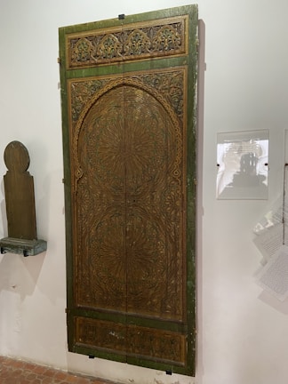 A beautifully carved teak wood door with colorful glass panels glowing in natural light.