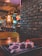 A cozy restaurant interior with dim lighting, featuring brick walls and wooden accents. In the foreground, a plate of sushi is elegantly presented with a small dish of soy sauce, placed on a dark wooden table. The background shows various colorful signs and ambient lights, creating a warm and inviting atmosphere.