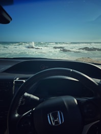 A driver holding a steering wheel with a calm ocean view through the windshield.