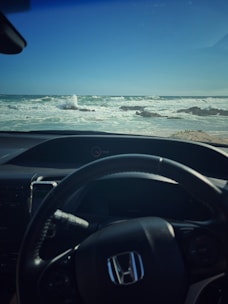 A driver holding a steering wheel with a calm ocean view through the windshield.