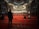 A spacious interior with ornate architectural details, featuring large chandeliers hanging from the ceiling, intricate arches, and vibrant red carpeting covering the floor. People are sitting and standing in various areas, likely engaged in prayer or contemplation.