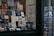 A bookstore window display with a variety of books and postcards. The books are neatly arranged on shelves with numerous titles visible, including travel guides and literature. Next to the display, there is a rotating stand filled with postcards featuring artistic and scenic designs.