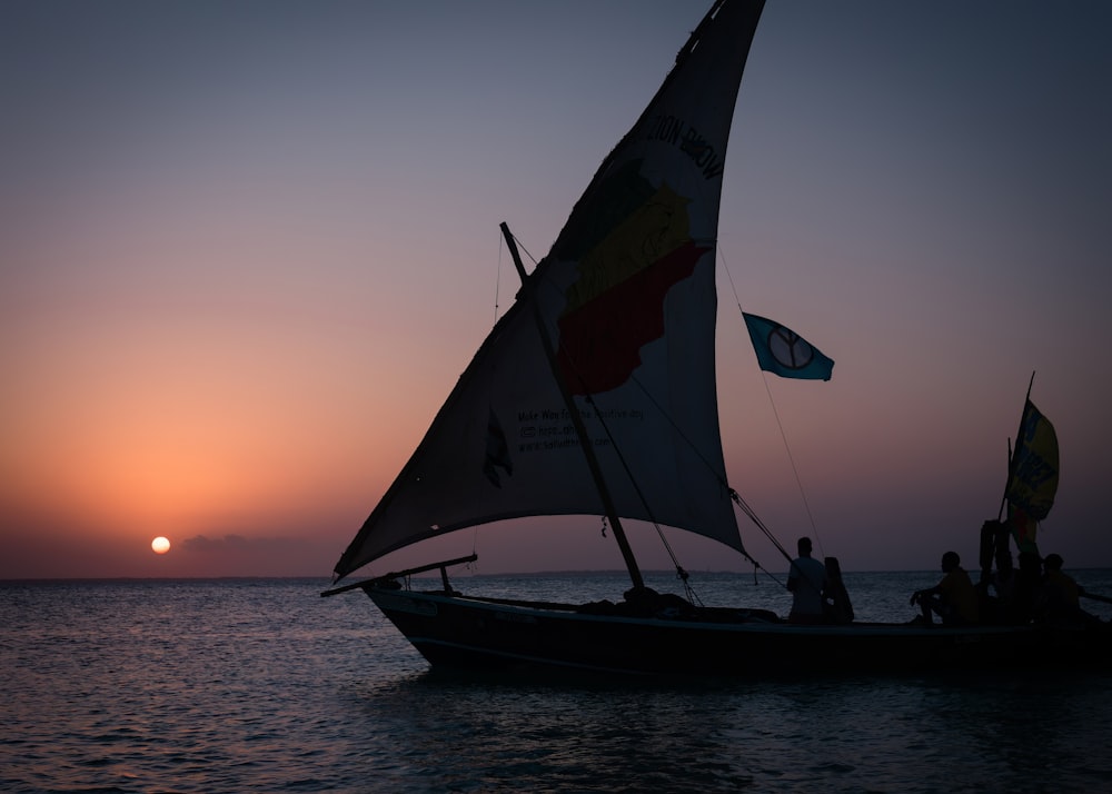 a sailboat with people on it in the ocean at sunset
