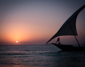 a person standing on a boat in the ocean at sunset