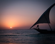 a person standing on a boat in the ocean at sunset