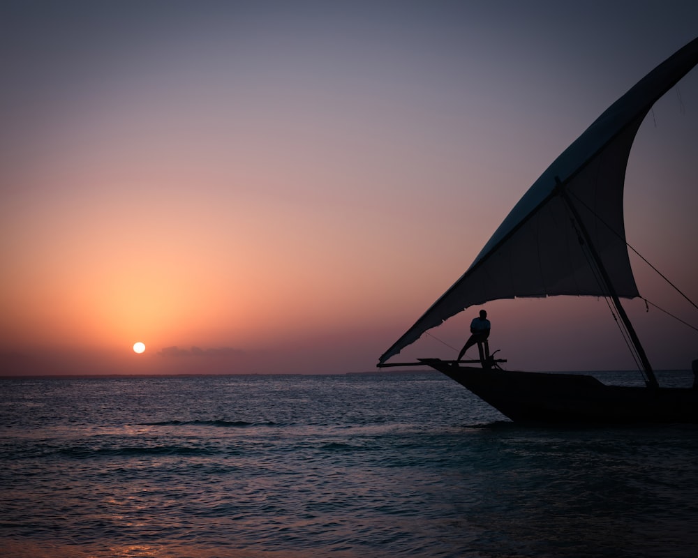 uma pessoa em pé em um barco no oceano ao pôr do sol