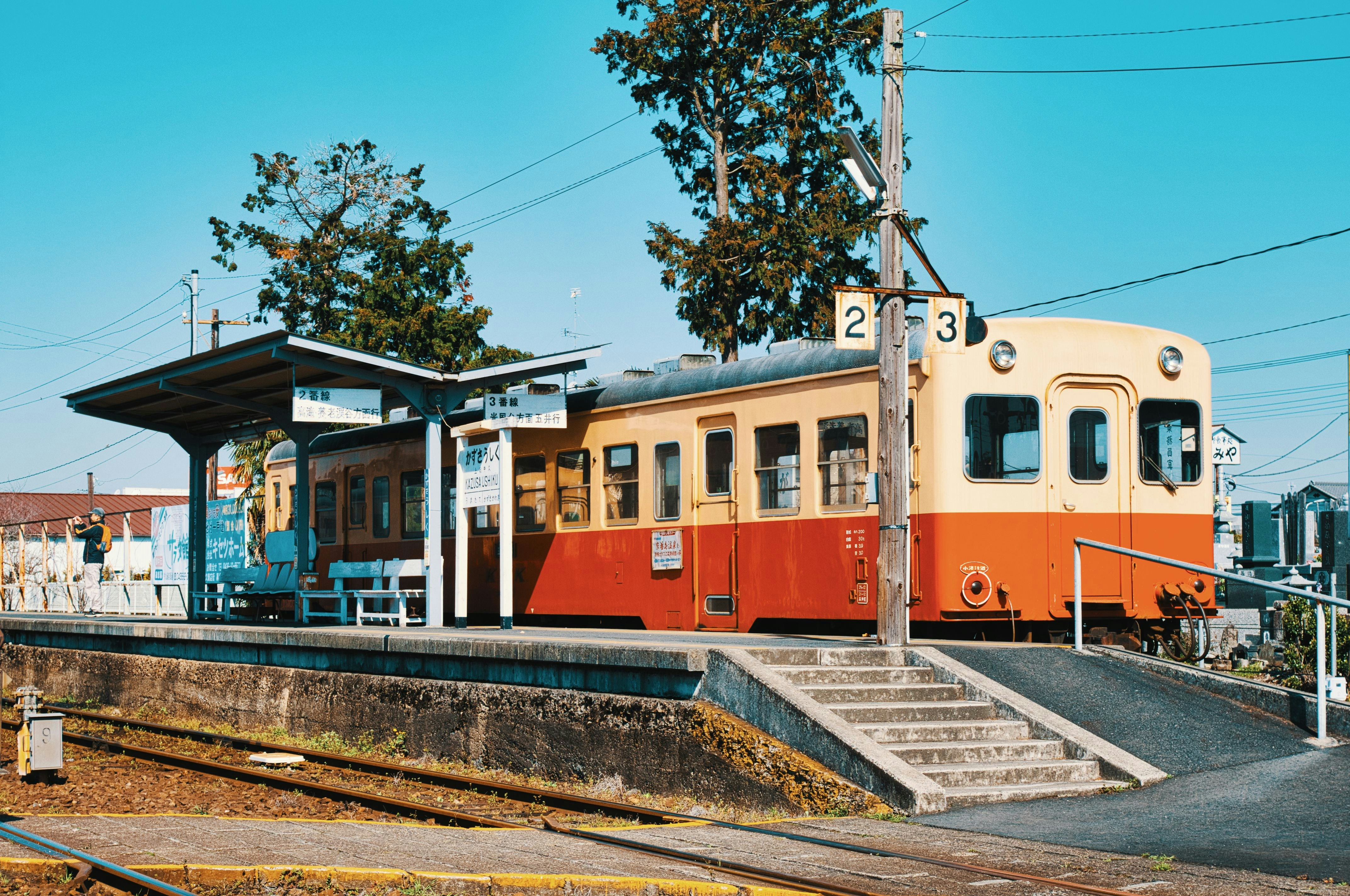 an orange and white train traveling past a train station