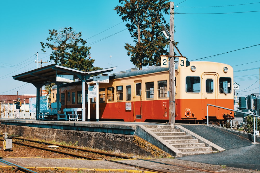 an orange and white train traveling past a train station