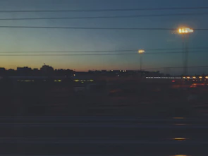 A horizontal cityscape at dusk with glowing lights and deep contrasts.