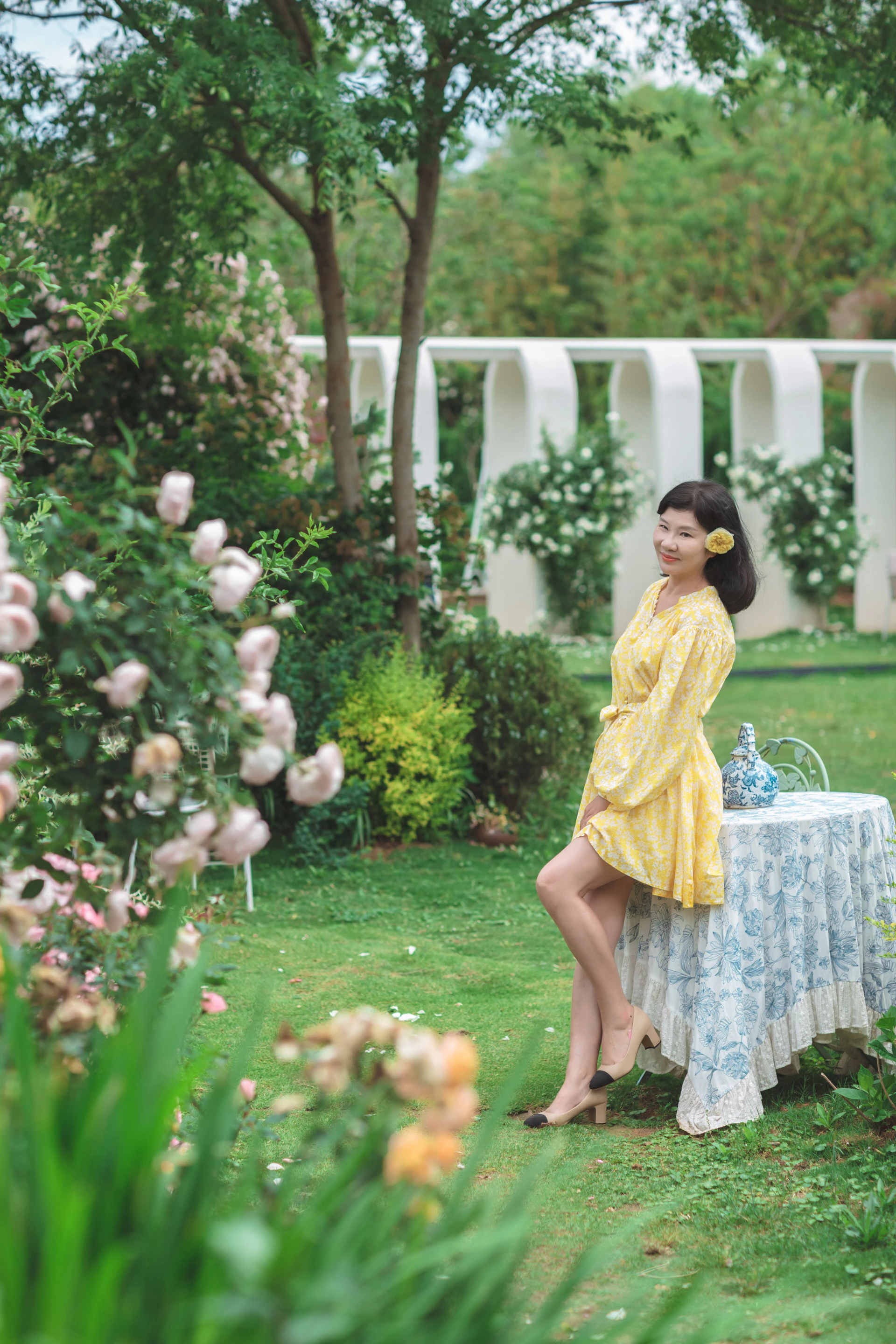 A vibrant photo of a model wearing a bright yellow summer dress from Solara Moda, standing in a sunlit urban park.