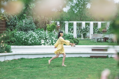 A young girl in a soft yellow dress with white polka dots, twirling around in a garden.