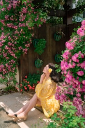 A serene woman sitting peacefully in a sunlit garden, surrounded by soft pink flowers.