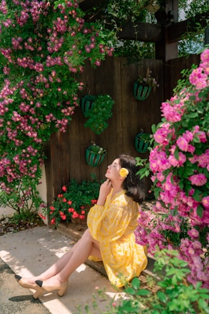 A serene woman sitting peacefully in a sunlit garden, surrounded by soft pink flowers.