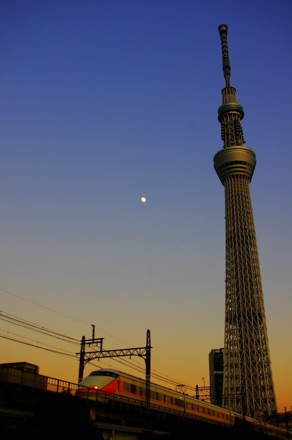 a train passing by a tall tower with a moon in the sky