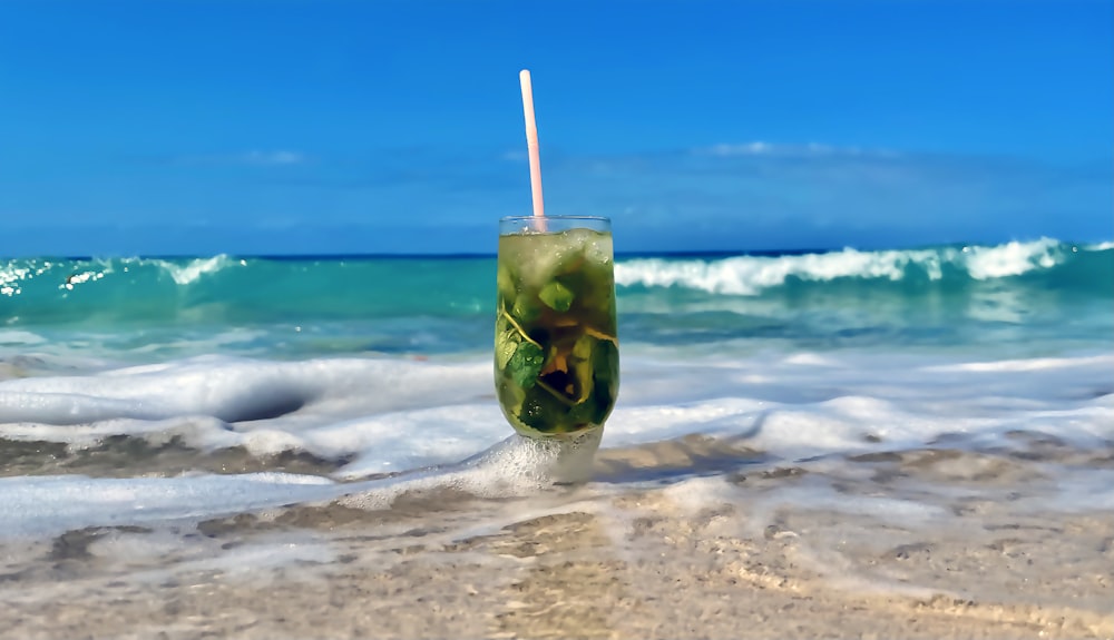 a drink with a straw in it sitting on the beach