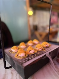 A culinary presentation of a dish displayed on a gridded platform with a backdrop of a softly lit interior. Each serving appears to have a creamy base topped with a delicate golden crispy element, possibly savory or sweet delicacies arranged artfully.