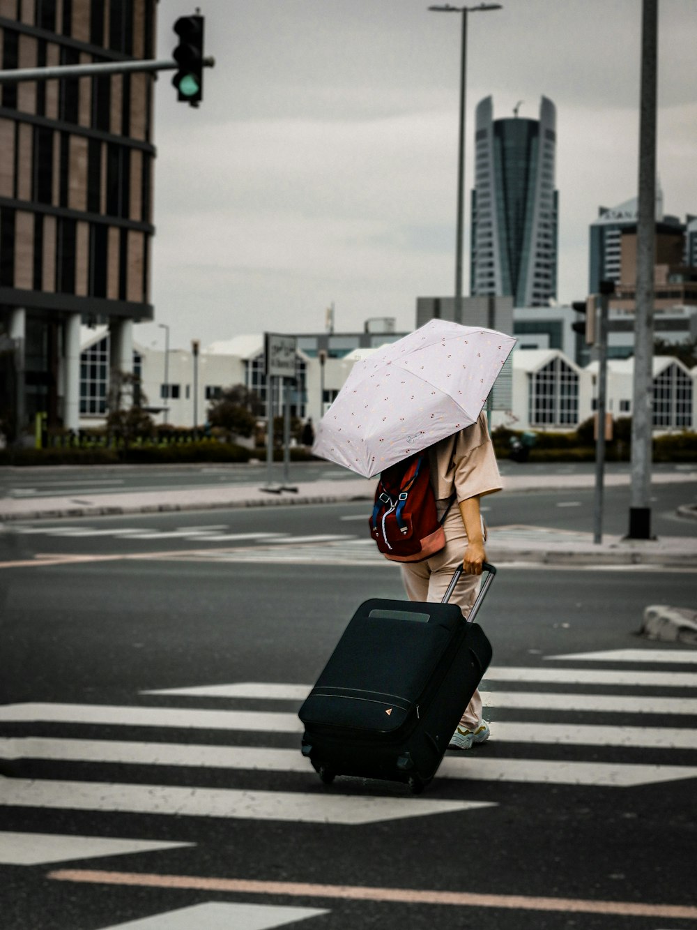 a person with an umbrella is pulling a suitcase across the street